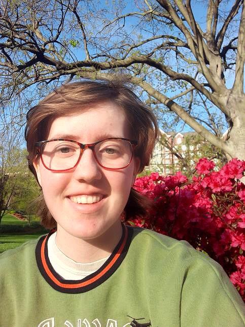 Person outside in front of a tree wearing glasses and a green top