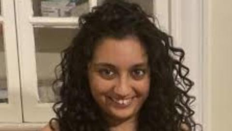Shraddha Lall with long, curly dark hair, wearing blue sleevless top, in front of whitecabinet