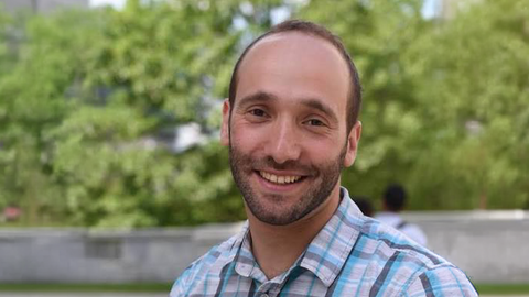 Man with a beard wearing a plaid shirt standing outside