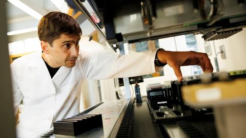 Michael Desai working in the lab wearing a white lab coat. Credit: Niles Singer