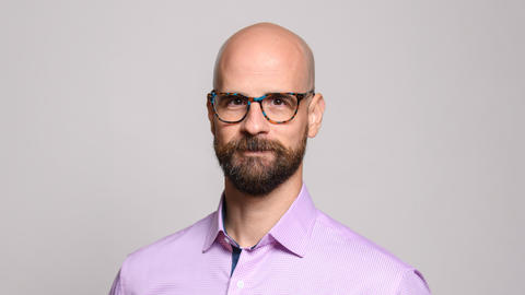 Portrait of Professor Javier Ortega-Hernandez wearing a pink shirt with glasses and a beard