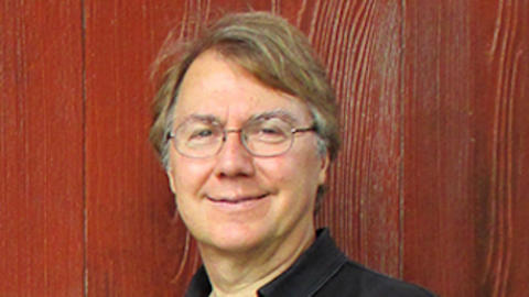 Portrait of Andrew Knoll wearing a black shirt and glasses in front of a red wall