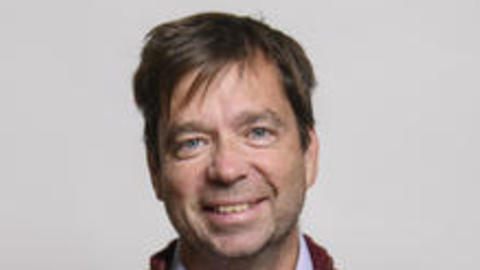 Bence Olveczky smiling, with short brown hair, a light purple shirt, and dark red sweater