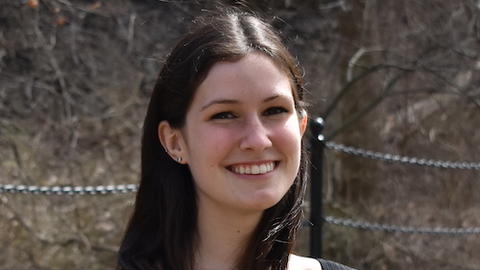 Kelsie Lopez with long brown hair and a black top, in front of bare branches and walkwayfence