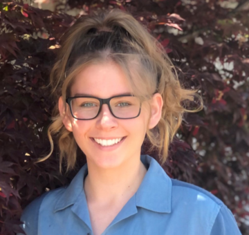 Woman outside wearing a ponytail, glasses and blue top