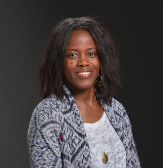 Mande Holford, smiling, with long dark hair and blue and white patterned tops, in front of dark background