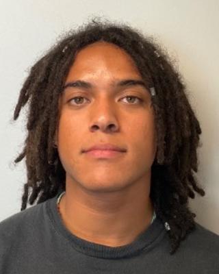 Gabriel Effiong with dark locs and a grey shirt, in front of a light grey background
