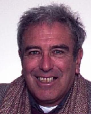 Joel Sohn with short grey hair, wearing a tweed sweater and jacket, in front of a white background