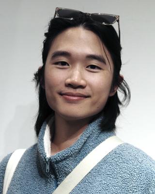 Chia-Wei Liu with long dark hair, sunglasses on head, and blue fleece, in front of grey background