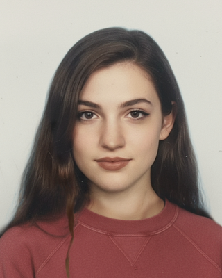 Anna Hatzakis with long brown hair and a red shirt, with a beige background