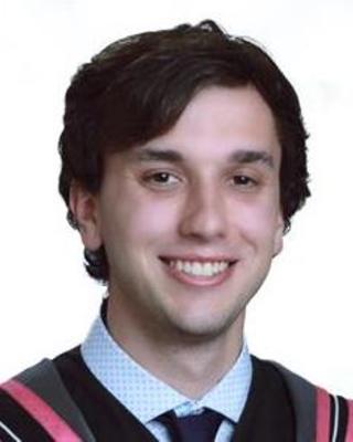 Ethan Mooney with short dark hair, checked shirt and blue tie, in front of white background