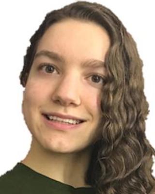 Lucia Gordon with long curly brown hair, a green shirt, and a white background