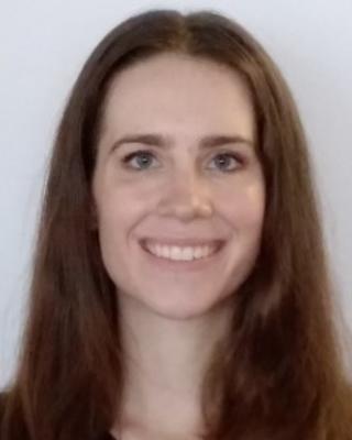 Fellow Lydia Zemke with long brown hair and dark top, in front of light grey background