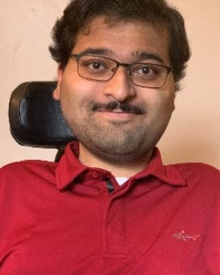 Rishab Kapoor with short dark hair and moustache, wearing glasses and red shirt, in a wheelchair