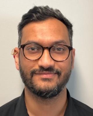 Saurabh Attarde with short dark hair and beard, wearing glasses, beige background