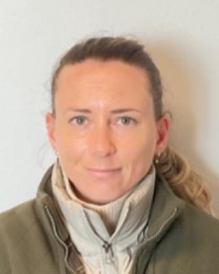 Vanessa Duthe, blonde hair pulled back, wearing a light green jacket, in front of a light grey background
