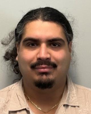 Christian Carrasco with brown hair, mustache and beard wearing a tan shirt