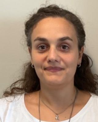 Federica Pizzulli with wavy brown hair pulled back, wearing a white top, on front of beige background