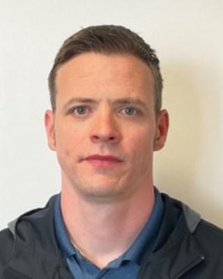 Portrait of James McKenna. Person with short dark hair wearing a black jacket and blue shirt