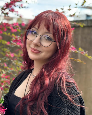 Headshot of Nat LaFont, woman with long red hair wearing glasses and standing outdoors