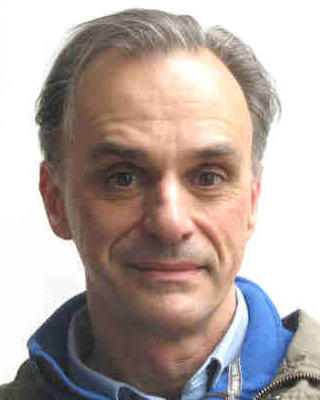 Portrait of postdoc Anthony Kiszewski wearing a blue shirt and gray jacket