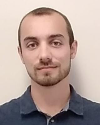 Portrait of postdoc Nicholas Russo with a beard wearing a blue shirt
