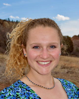 Woman with blonde curly hair in a ponytail standing outside and smiling