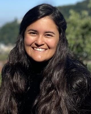 Woman with long dark hair sitting outside and smiling