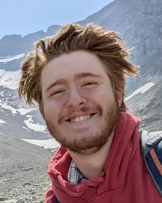 Man with red hair wearing a red jacket standing in front of a mountain