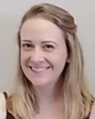 Allison Kann with long blonde hair half up, red sleeveless shirt, grey background