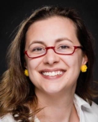 Amie Jones smiling with long brown hair, red glasses, white shirt, black background