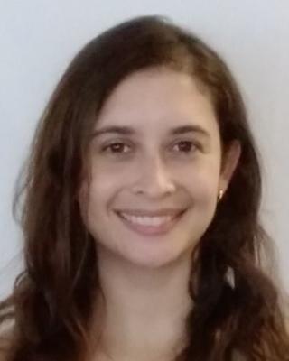 Andrea Unzueta Martinez with long wavy brown hair, in front of light grey background