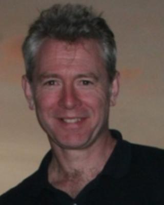 Andrew J. Berry with short grey hair, dark polo, and beige background
