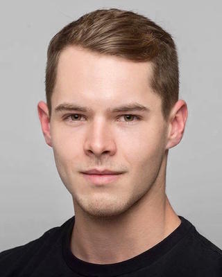 Austin Garner with short brown hair, wearing black shirt, in front of grey background