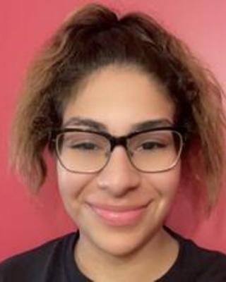 Breanna Jordan wth long brown hair pulled up, wearing glasses and a lack top, in front of a red background