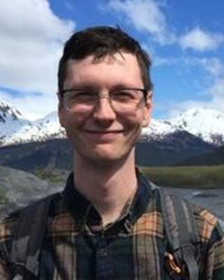 Calvin Heslop with short brown hair and glasses, wearing a plaid shirt, in front of distant snowy mountains