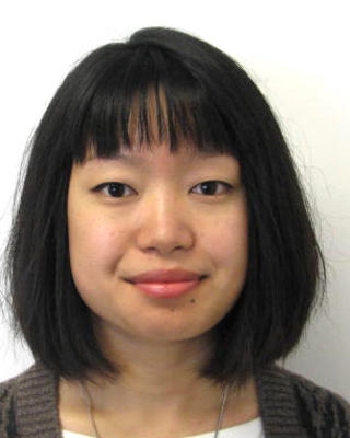 Caroline Hu with shoulder length black hair, wearing a grey and black cardigan, in front of a light grey background