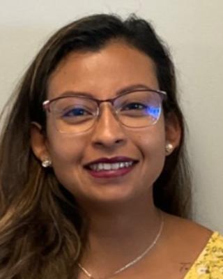 Catlina Romero Ortiz with long brown hair, glasses, and a yellow top, in front of beige background