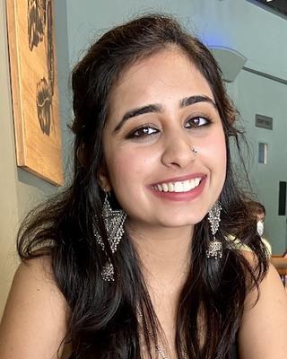 Cheshta Bhatia with long dark hair, in front of sage green hallway with woodpabel artwork