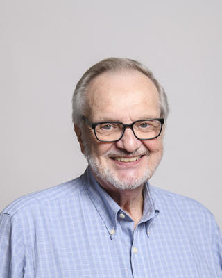 Dan Hartl with gray hair and a beard wearing glasses and a blue shirt