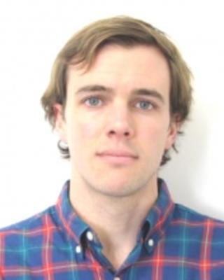 Daniel Hoer with short light brown hair, wearing a blue and red plaid shirt, in front of a white background