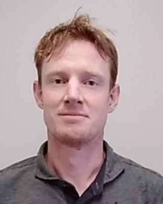 Dawson White with short red hair and goatee, wearing grey shirt, in front of light grey background