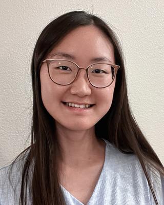 Duyi (Tina) Kuang with long dark hair, wearing glasses and a light grey shirt, in front of a beige wall