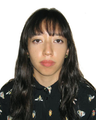 Edna Rodriguez with long dark hair and bangs, with black patterned shirt, in front of white background