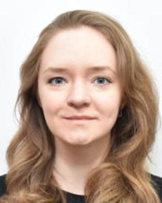 Evgenilia (Jenya) Belousova with long dark blonde hair and black top, in front of white background