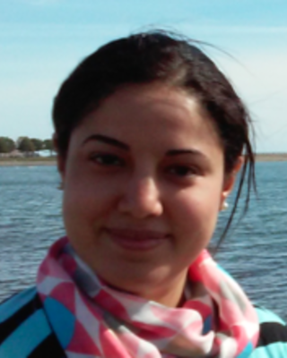 Fatma Gomaa with dark hair pulled back, wearing a pink patterend scarf and blue striped shirt, with water and sky in the background