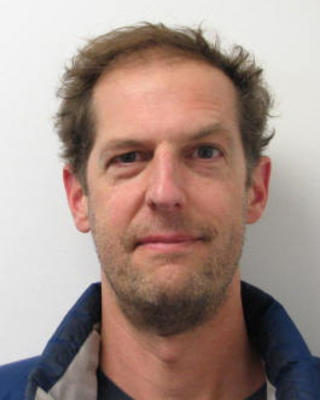 Fulton Rockwell with short brown hair and beard, wearing blue coat, in front of light grey background