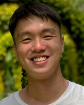 Galen Tiong with short dark hair, wearing a white top, with green leafy trees in the background