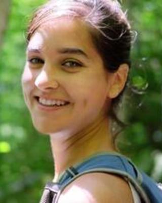 Inbar Maayan smiling, dark hair pulled back, wearing a backpack, in a forest
