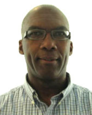 Irv Dumay with black glasses, light check shirt, white background